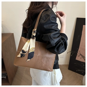 Detail of brown patchwork tote bag with snake texture and decorative silk scarf on shoulder
