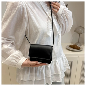 Close-up of minimalist black matte faux leather mini flap crossbody bag worn by model