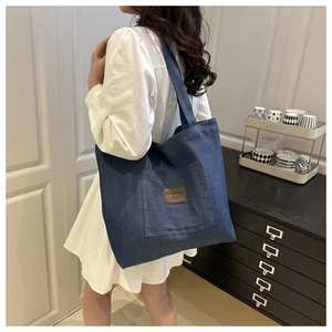 Detail of dark blue denim tote bag with leather tag on model in indoor setting