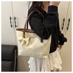 Detail of a creamy white tote bag with brown straps and a cute dog charm on a model