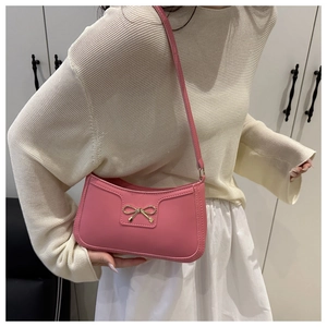 Detail of pink PU shoulder bag featuring a gold metal bow buckle and a smooth zipper closure