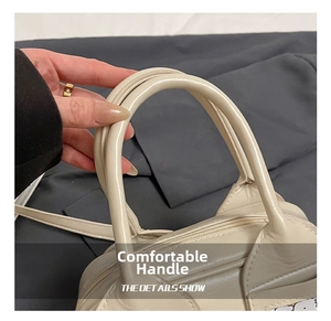 Détail montrant les doubles poignées lisses et le zip métallique du sac Boston blanc cassé