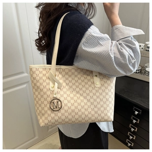 Detail view of cream tote bag with letter M jacquard pattern and metallic charm