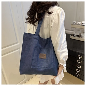 Detailed shot of dark blue denim tote bag with leather logo patch and front pocket