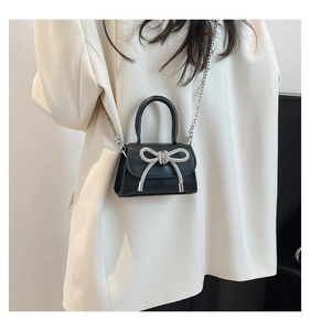 Detail of a black leather mini bag with rhinestone bow and silver chain strap