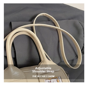 Détail du sac Boston en cuir crème montrant les poignées et la bandoulière réglable