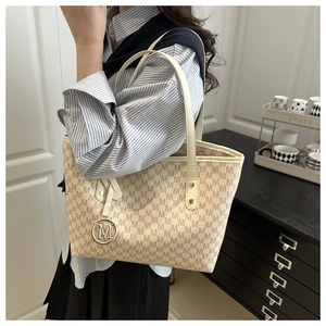 Close-up of beige tote bag with brown M pattern and round metallic logo pendant