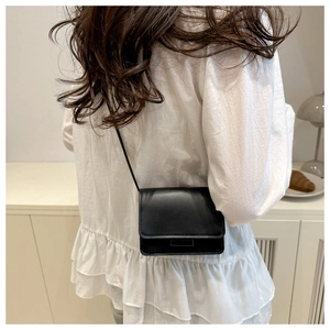 Detailed view of a small black leather crossbody bag worn by a model in a cozy home setting
