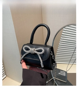 Close-up of black leather mini handbag featuring a large sparkling rhinestone bow and chain