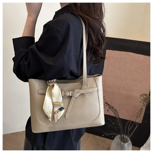 Chic khaki tote bag with decorative silk scarf on handle worn by model indoors