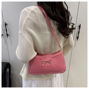 Close-up of pink crescent underarm bag with gold bow clasp on cream knit outfit