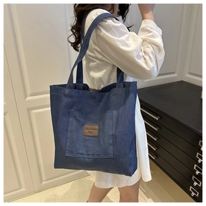 Détail d'un grand sac cabas en denim bleu foncé avec un patch en cuir et une bandoulière chic