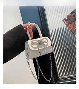 Close-up of mini white leather bag with silver rhinestone bow and chain strap