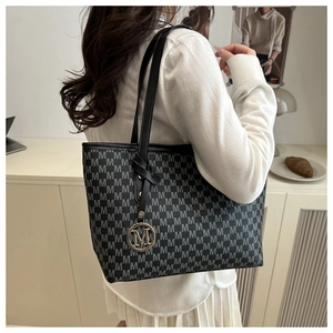 Close-up of letter pattern texture and metallic M-shaped pendant on grey tote bag