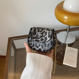 Mini-Satteltasche mit Leopardenmuster und goldener Kette vor warmem Hintergrund
