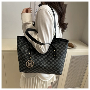 Detail of black monogram tote bag with gold M-logo charm shown in a lifestyle setting
