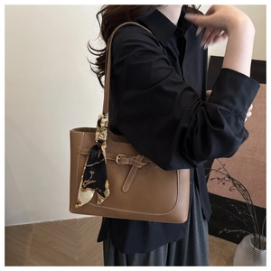 Detail of brown tote bag featuring decorative strap and elegant patterned silk scarf handle