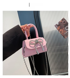 Detail of pink mini handbag featuring a large rhinestone bow and silver chain strap