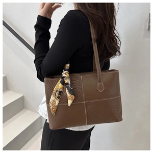 Detail of a brown leather tote bag with reptile texture stitching and a silk scarf handle