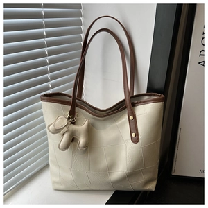 Detail of a large cream tote bag with brown trim and cute dog pendant in window light