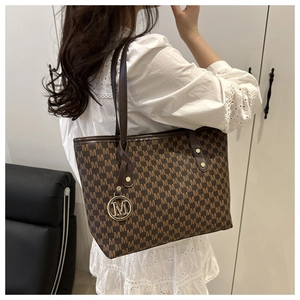 Detailed side view of brown tote bag with M-pattern and metallic logo pendant