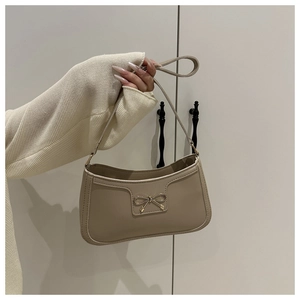 Detail of a khaki leather underarm bag with a golden metal bow ornament on the side
