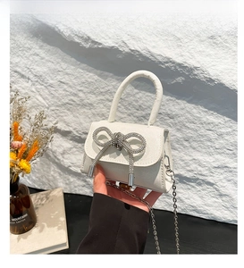 Detail of white mini bag with sparkling rhinestone bow and silver metal chain strap