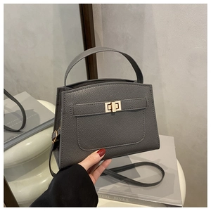 Detail of grey pebbled leather handbag with gold rectangular twist lock on a white stand