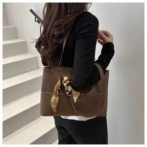Detail of leather patchwork tote bag with snake texture and decorative silk scarf