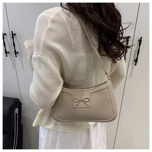 Close-up of beige underarm bag featuring a delicate golden bow buckle on smooth leather