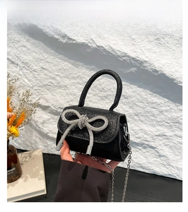 Detail of a black glitter mini handbag featuring a crystal bow and silver chain strap