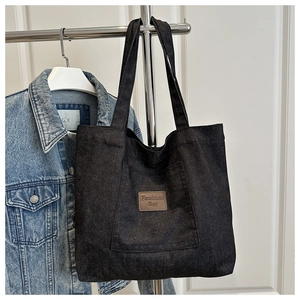 Détail du sac cabas en denim noir avec écusson en cuir et poche frontale pratique