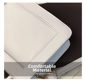 Close-up of white glossy faux leather handbag with precise stitching and gold metal buckle