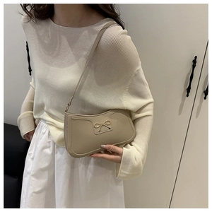 Detailed view of beige crescent bag with golden bow buckle on model shoulder