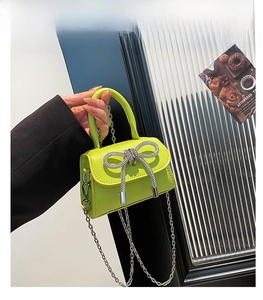 Detail of neon green mini bag with silver rhinestone bow and metal chain strap