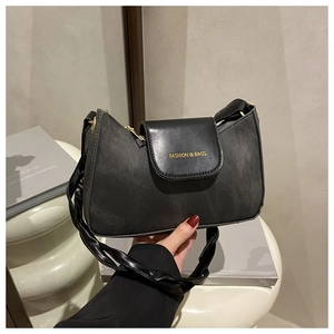 Détail du sac sous le bras en cuir noir mat avec logo doré et bandoulière tressée