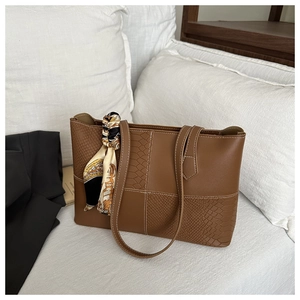 Detail of a brown faux leather tote bag with crocodile texture and silk scarf handle accent