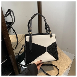 Close-up of black and white patchwork handbag with woven texture and gold rivets