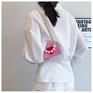 Detail of pink mini bag with red heart, pearl handle and gold chain strap on model
