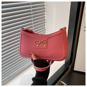 Detail of pink PU underarm bag featuring a gold metal bow and thick contrast stitching
