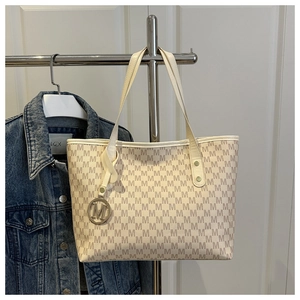 Detail of cream tote bag featuring brown M-monogram pattern and gold circular charm