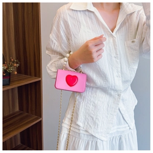 Close-up of pink heart-shaped mini crossbody bag with pearl handle and gold chain