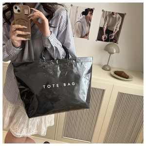 Close-up of black glossy tote bag with white TOTE BAG lettering and sturdy handles