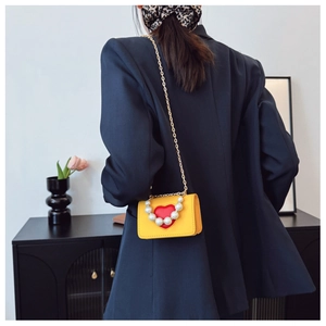 Détail d'un sac jaune à cœur avec poignée en perles et chaîne dorée sur mannequin