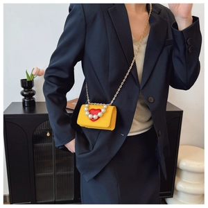 Detail of yellow mini crossbody bag with red heart, pearl handle, and golden chain strap