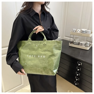 Close-up of green crinkled tote bag with white text held in a minimalist room