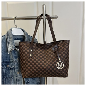 Close-up of brown tote bag with M-letter monogram pattern and round logo charm detail