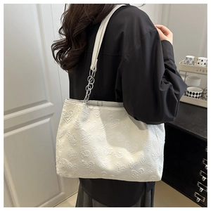 Shoulder bag featuring embossed heart pattern and metallic chain strap on model