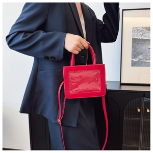Detail of red crossbody bag with clear window panel and adjustable strap shown on model