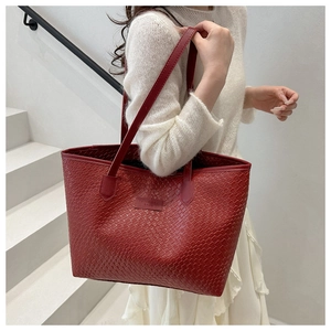 Close-up of red woven leather tote bag with branded logo patch and shoulder strap detail